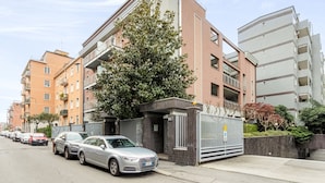 A modern apartment building with a gated entrance, parked cars, and a tree in front. - Candiani F1 Bilocale (Milan)