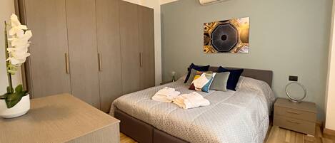 A bedroom with a bed, bedside table, nightstand, wardrobe, and a wall-mounted air conditioner.