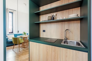 Una cocina moderna con armarios de madera, un lavamanos de acero inoxidable y una zona de comedor con un sofá azul y una silla verde.