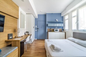 A modern hotel room with a wooden desk, a bed, a TV, and a kitchenette. - Gran Sasso - Cozy Modern Studio Steps From Piazza Piola (Milan)