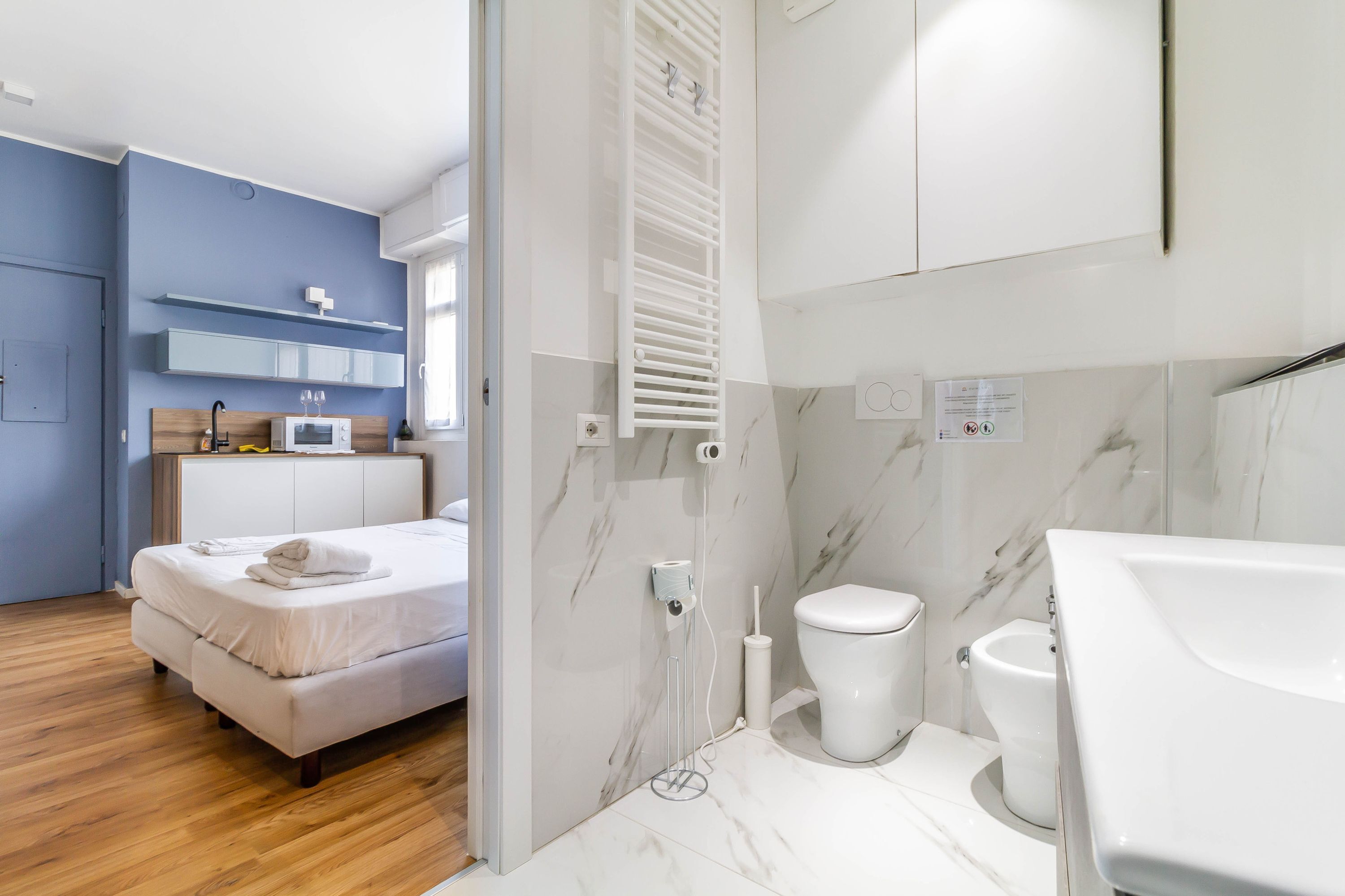 A modern hotel room with a bed, a white toilet, and a bathroom with a white sink and mirror.