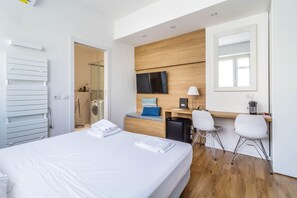 A modern hotel room with a neatly made bed, a desk with a computer, a TV, and two chairs. - Gran Sasso - Cozy Modern Studio Steps From Piazza Piola (Milan)