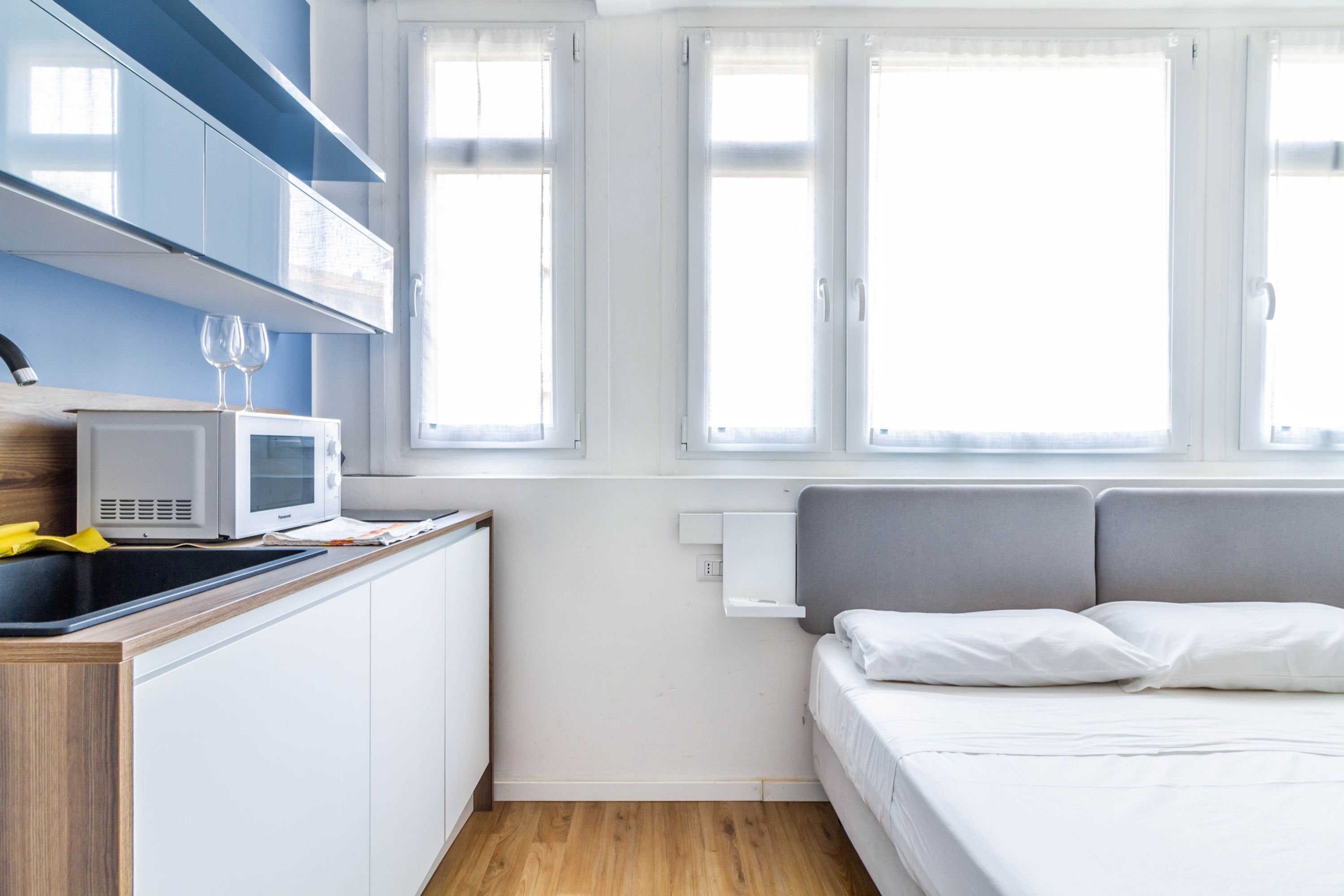 Ett kompakt hotellrum med ett litet pentry, en säng med vita sängkläder och ett fönster med utsikt.