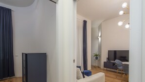A modern living room with a sofa, a small table with a plant, a TV, and a dining area with chairs. - Porta Vittoria - Cozy Stylish 1bdr in Duomo San Babila Area (Milan)