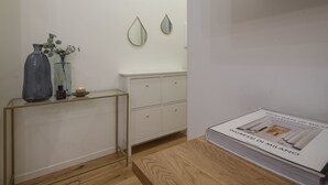 A minimalist room with a wooden floor, a white cabinet, a glass console table with decorative items, and a book titled "INGRESSI DI MILANO" on a wooden table. - Porta Vittoria - Cozy Stylish 1bdr in Duomo San Babila Area (Milan)