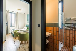 A modern hotel room with a dining area, a bathroom with a tiled shower, and a view of the outside. - Quantum 2 Quarks in Milano (Milan)