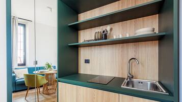 A modern kitchen with wooden cabinetry, a stainless steel sink, and a dining area with a blue sofa and a green chair.
