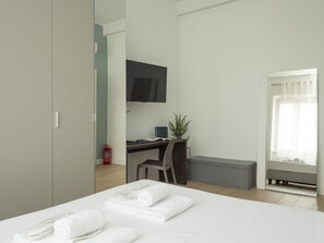 Une chambre d’hôtel moderne équipée d’un lit, d’un bureau, d’une chaise, d’une télévision et d’une fenêtre avec des rideaux.