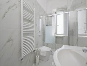 Une salle de bain moderne avec une douche à parois de verre, un lavabo blanc et des murs en marbre.