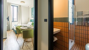 Une chambre d'hôtel moderne dotée d'un coin repas, d'une salle de bain avec douche carrelée et d'une vue sur l'extérieur.