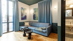Un salon moderne avec un canapé, deux tables d’appoint et une grande fenêtre agrémentée de rideaux.