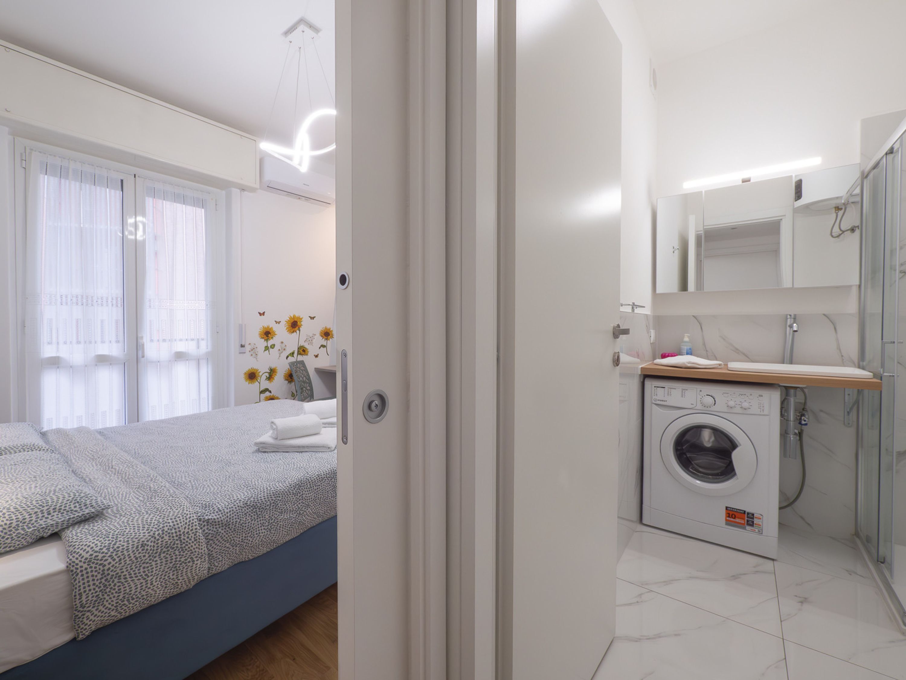 Ein modernes Schlafzimmer mit einem Bett, einer Waschmaschine und einem durch eine offene Tür einsehbaren Badezimmer.