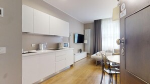 Una cocina moderna con armarios blancos, un microondas y un televisor de pantalla plana. Hay una zona de comedor con una mesa y sillas.