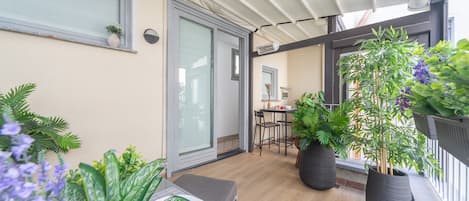 Un balcon avec une table dressée pour les repas, des plantes en pot et une porte-fenêtre coulissante donnant sur un espace intérieur.