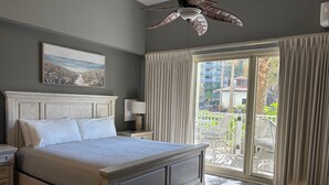 Ein Schlafzimmer mit einem großen Bett, einem Deckenventilator, einem Gemälde an der Wand und Blick auf den Balkon.