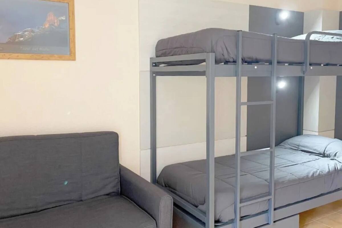 A bunk bed with a grey mattress, a grey sofa, and a framed picture on the wall.