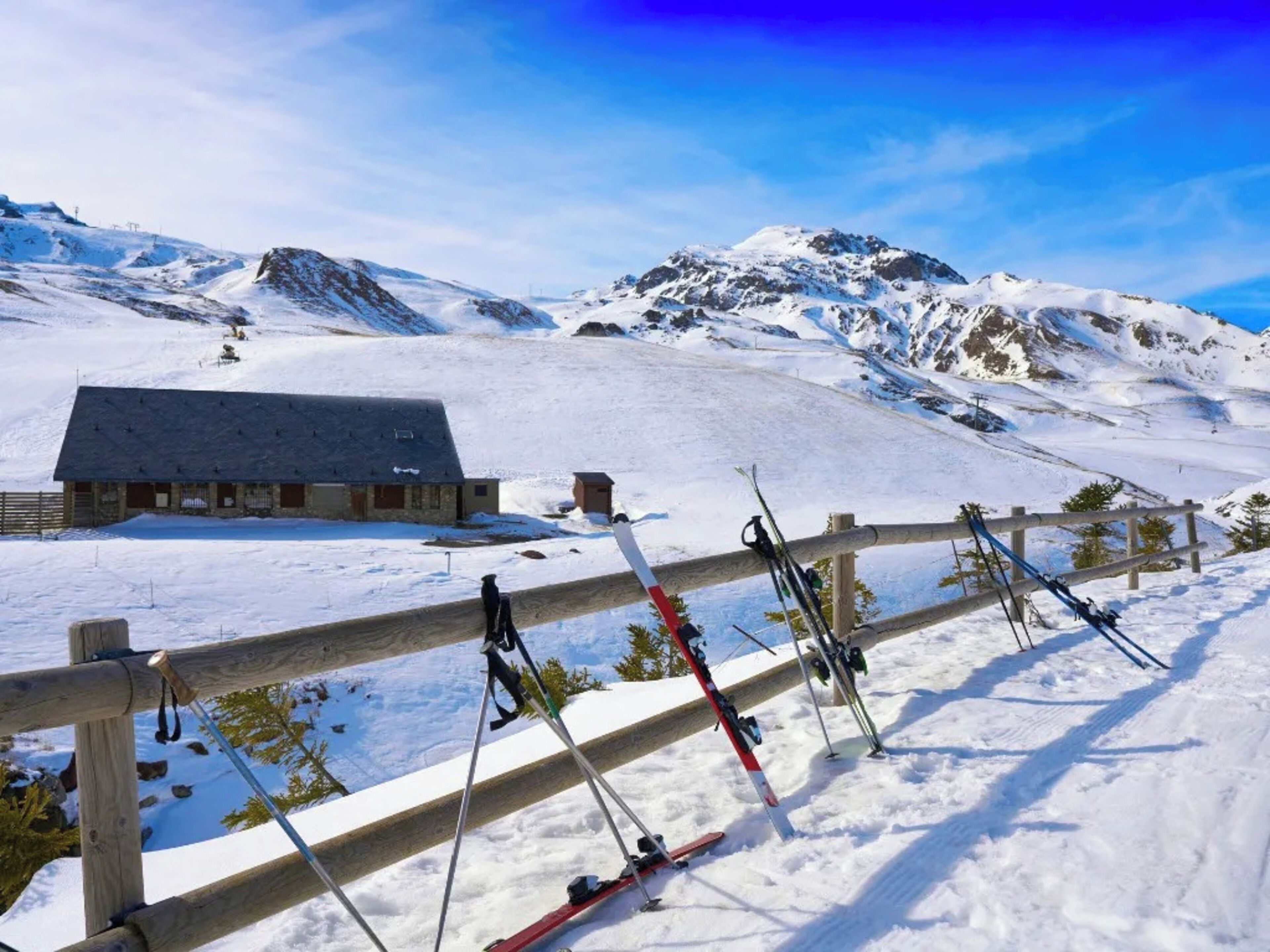 A snow-covered mountain with a wooden fence and skis leaning against it.