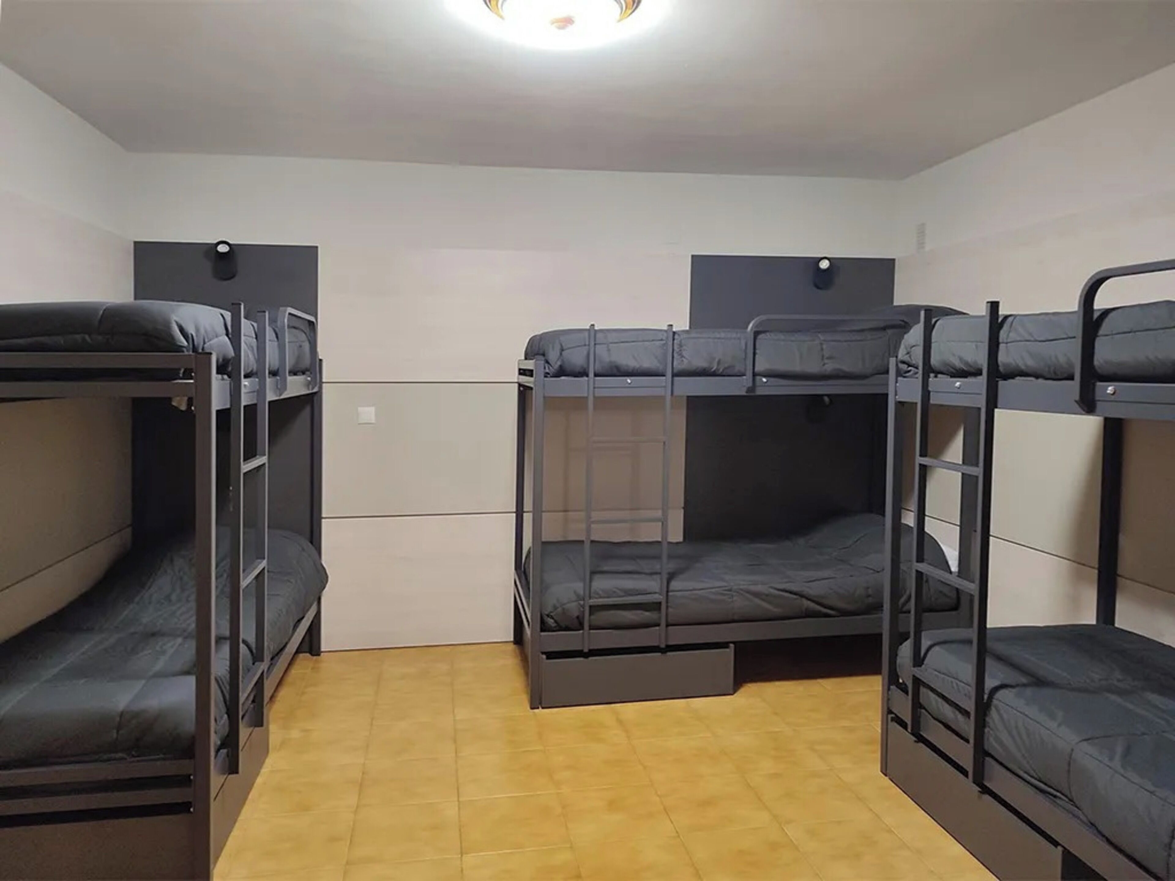 Une chambre de dortoir avec des lits superposés, un petit bureau et un sol carrelé.