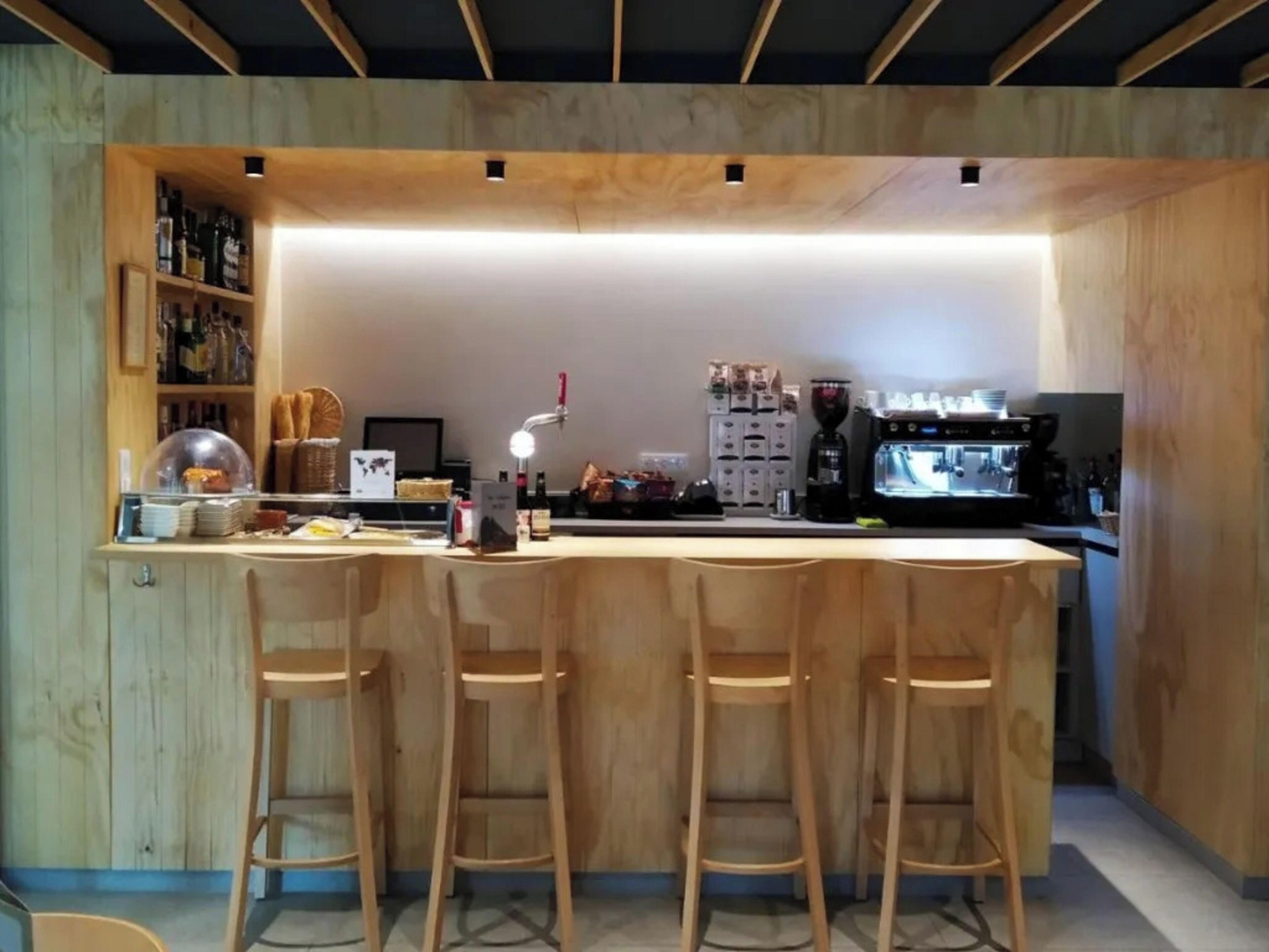A modern kitchen with a wooden bar area, bar stools, and a coffee machine.