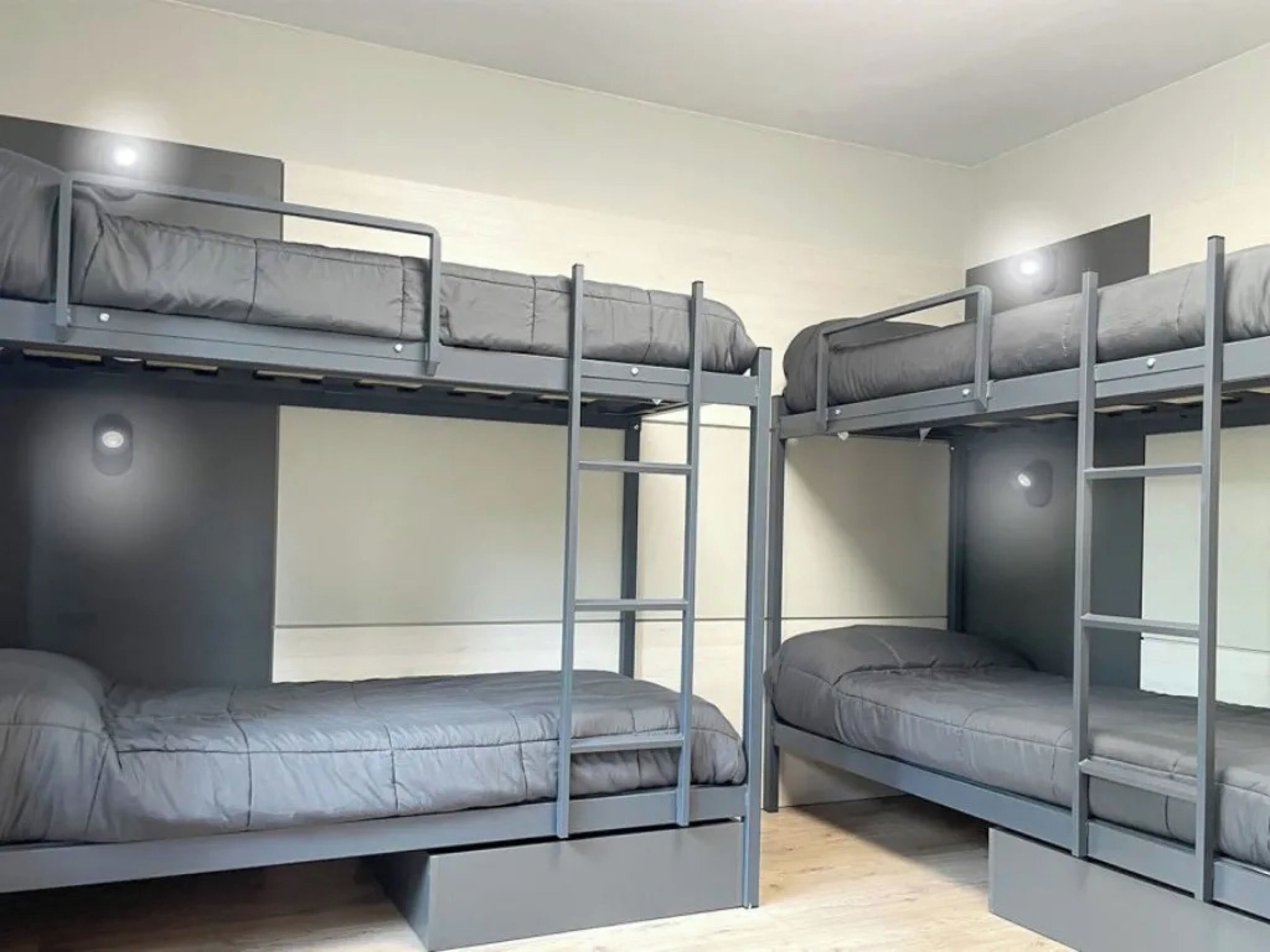 Une chambre de type dortoir avec des lits superposés, chacun étant équipé d’un matelas et d’un oreiller. Une échelle est placée entre les lits pour permettre d’accéder au lit supérieur.