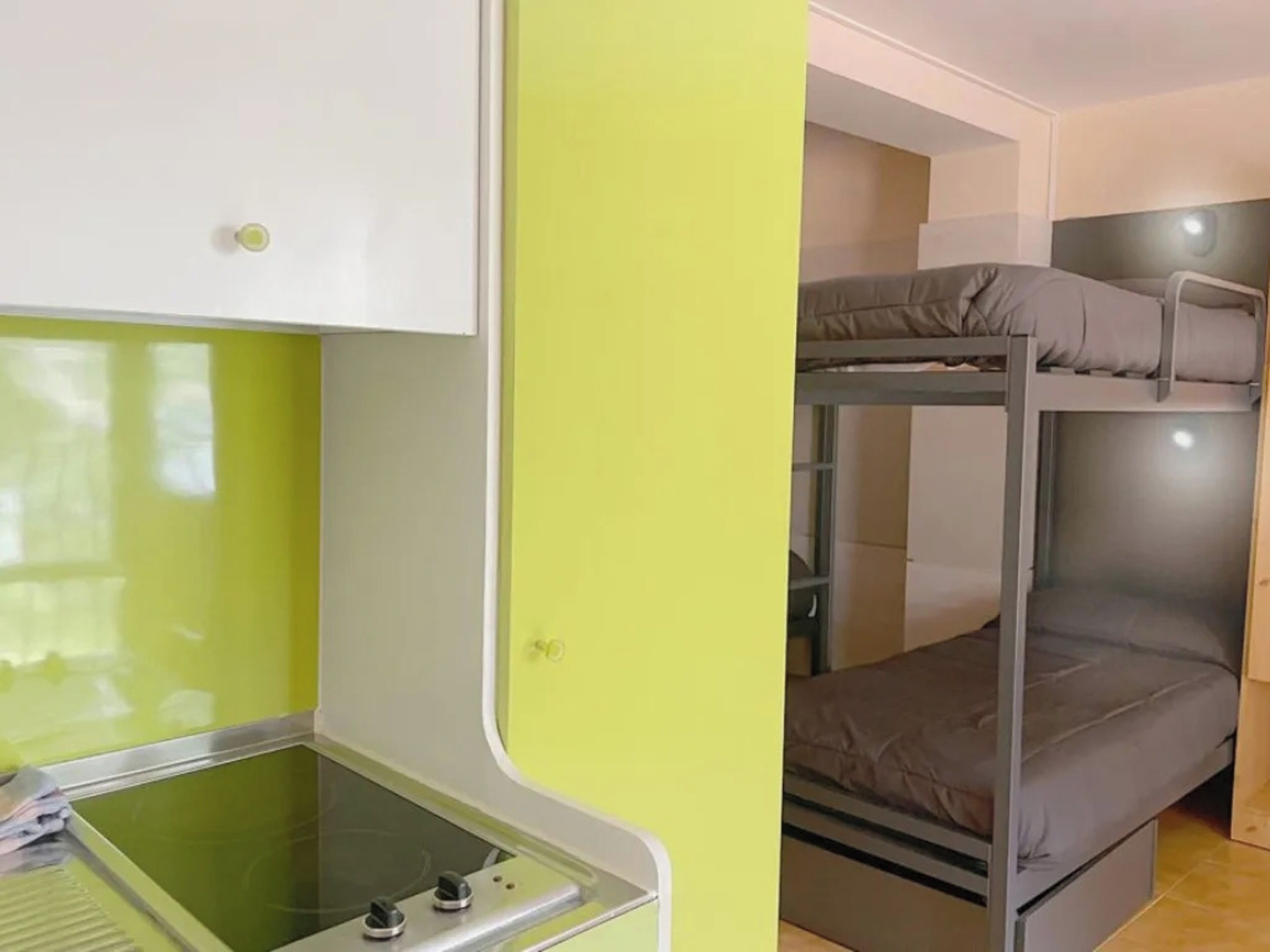 Een slaapkamer met een stapelbed, een groene muur en een kleine kitchenette.