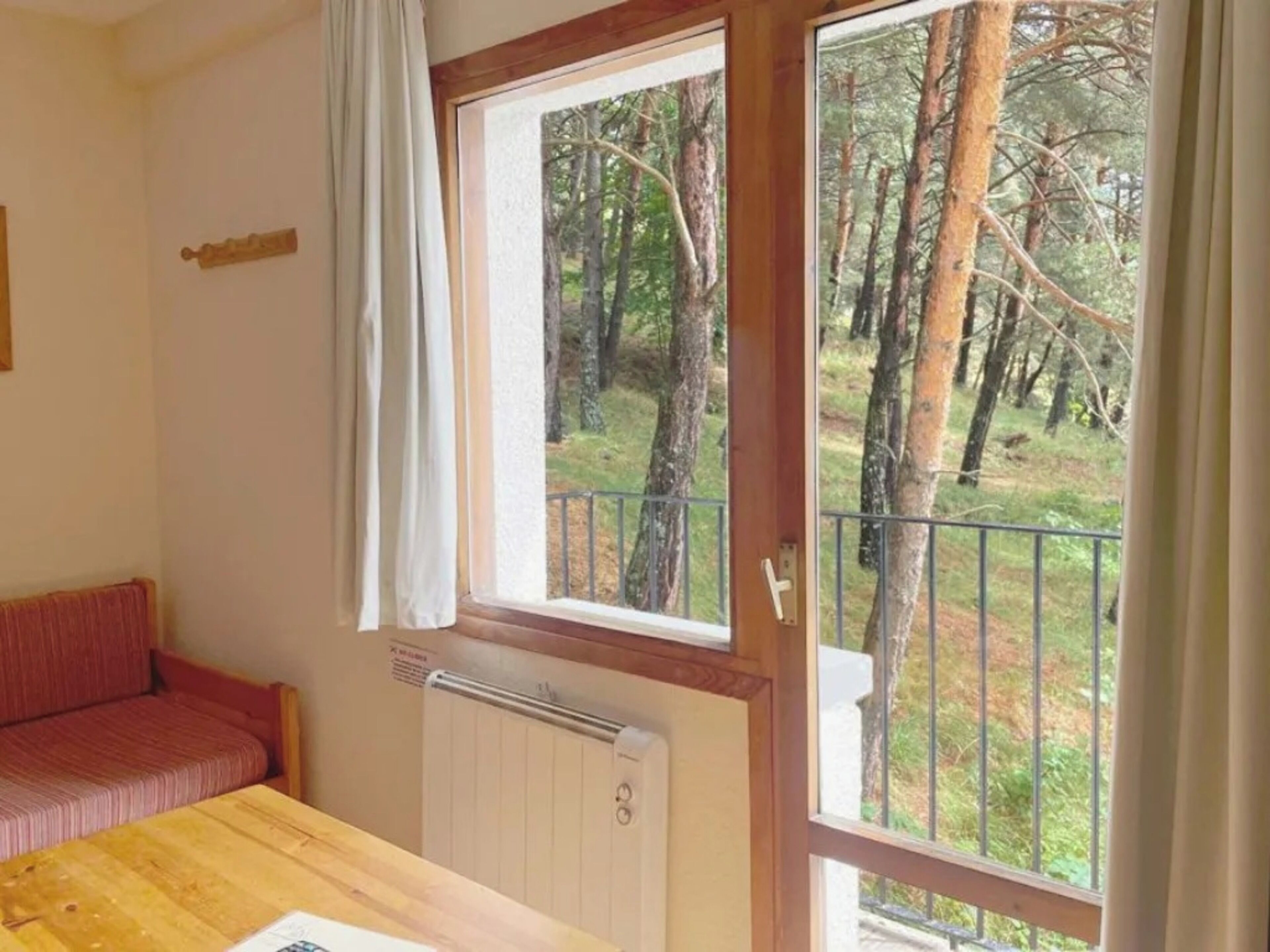 Une pièce avec une table en bois, un canapé rouge, une fenêtre donnant sur des arbres et un radiateur.