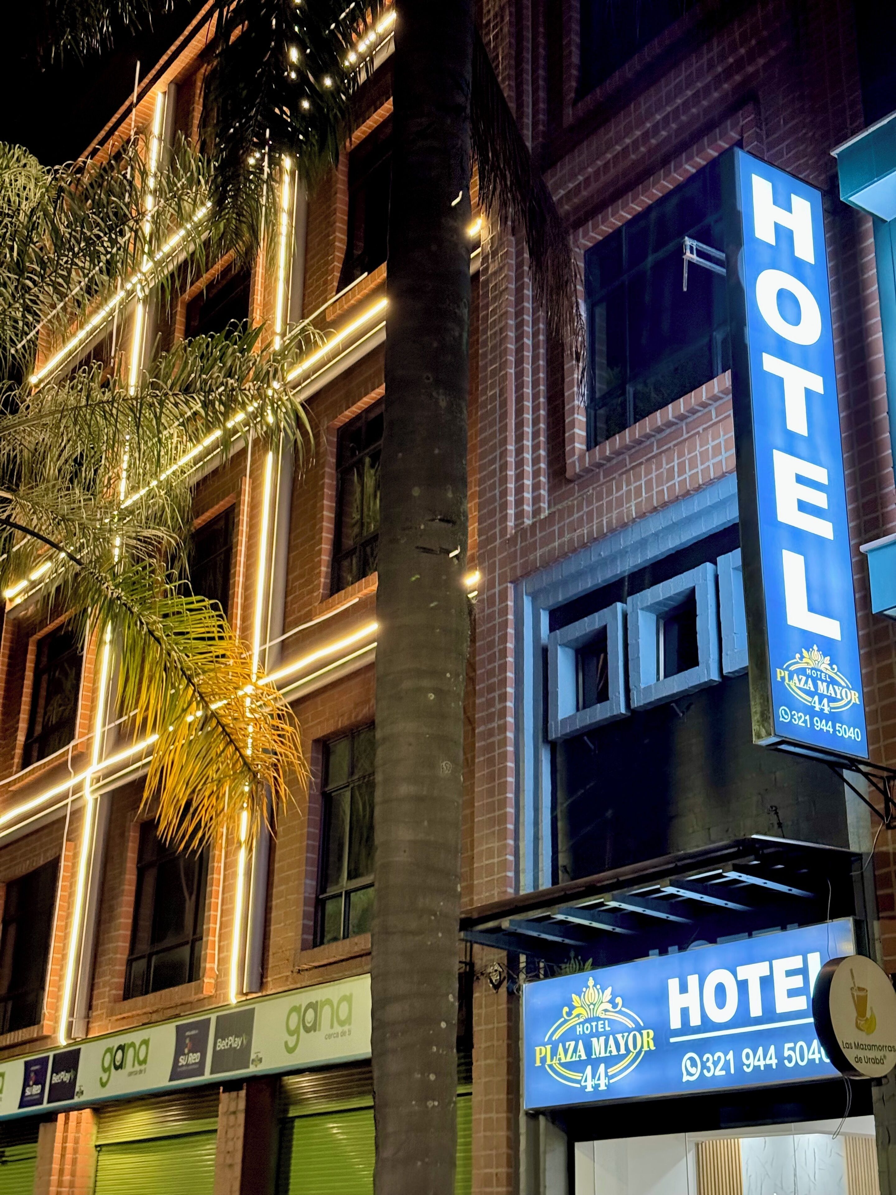 A hotel with a prominent 'HOTEL' sign, a 'Plaza Mayor' sign, and a contact number.