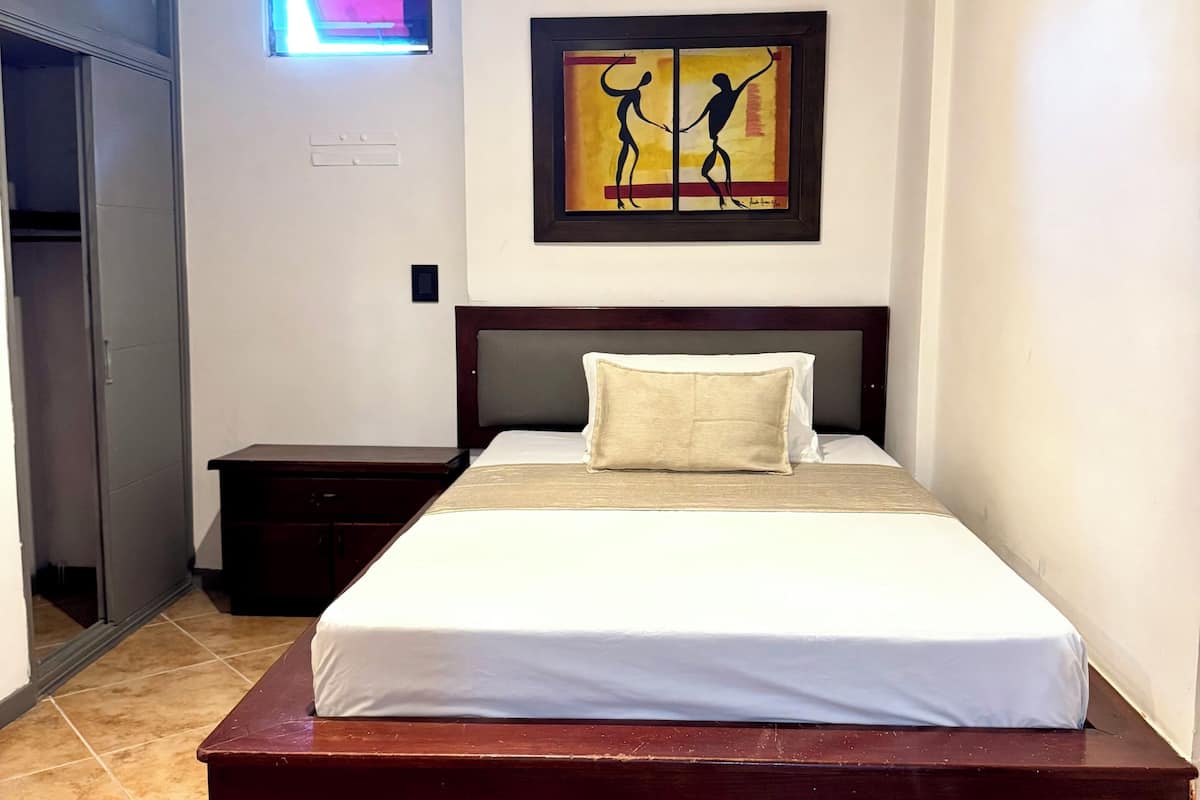 Une chambre à coucher avec un grand lit, une table de chevet, une armoire et une œuvre d’art accrochée au mur.