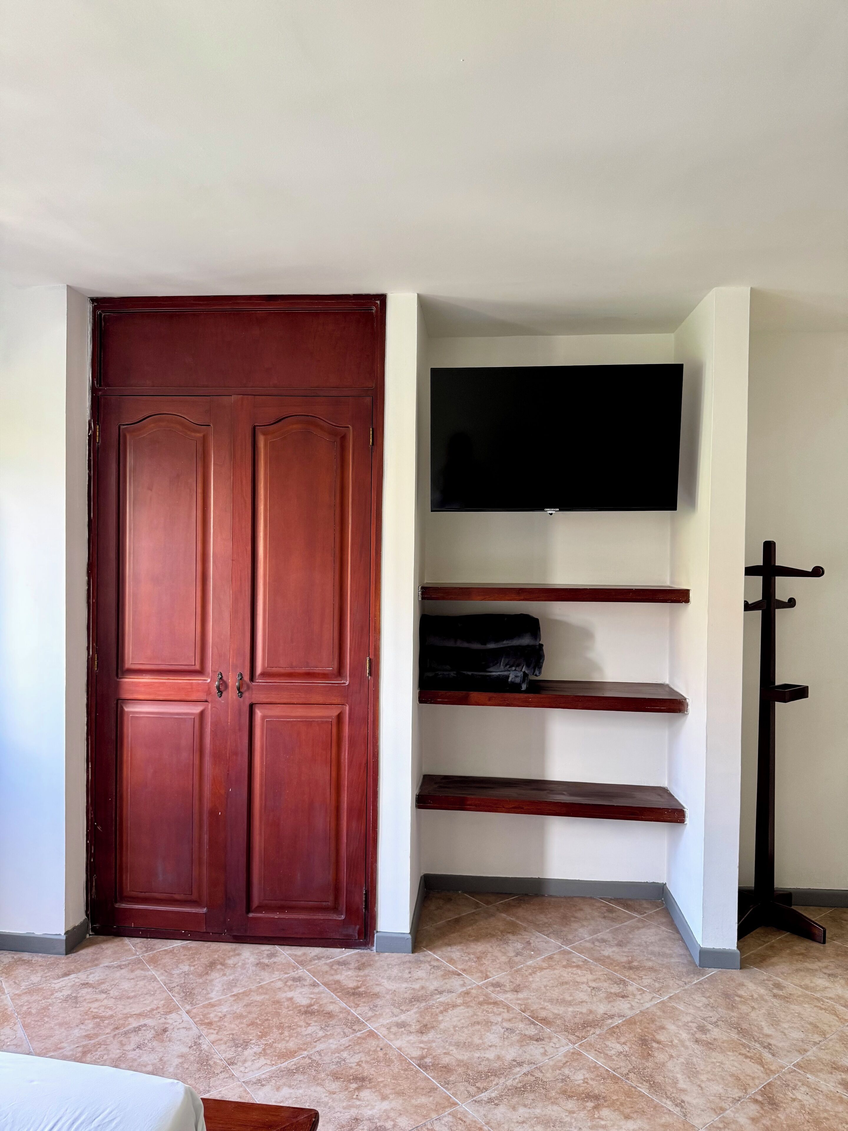 A room with a wooden wardrobe, a flat-screen TV mounted on the wall, and a coat rack.