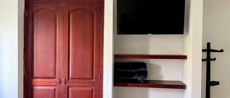 A room with a wooden wardrobe, a flat-screen TV mounted on the wall, and a coat rack.