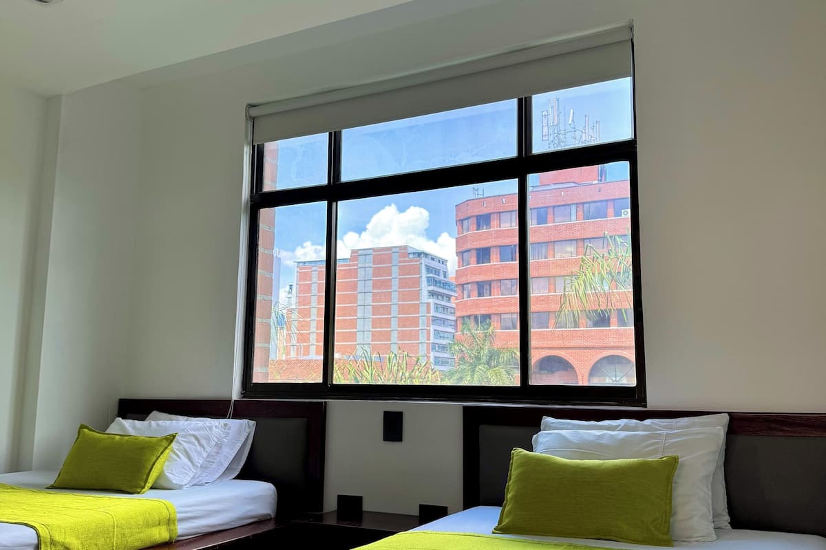 Une chambre d’hôtel avec deux lits, une grande fenêtre et une vue sur les immeubles.