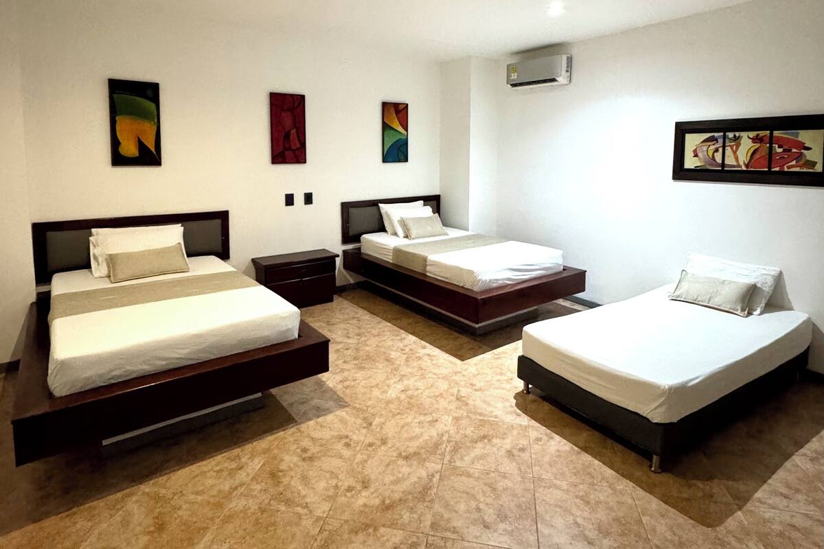 Une chambre d’hôtel avec trois lits disposés en forme de U, une grande fenêtre et un téléviseur à écran plat fixé au mur.