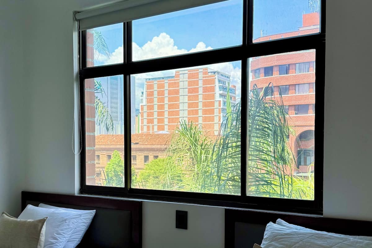 Une chambre d’hôtel avec deux lits, une grande fenêtre donnant sur des immeubles et des arbres, et une petite table de chevet.