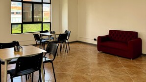 Una habitación amplia con comedor, un sofá rojo y ventanas grandes con vistas a edificios y zonas verdes.
