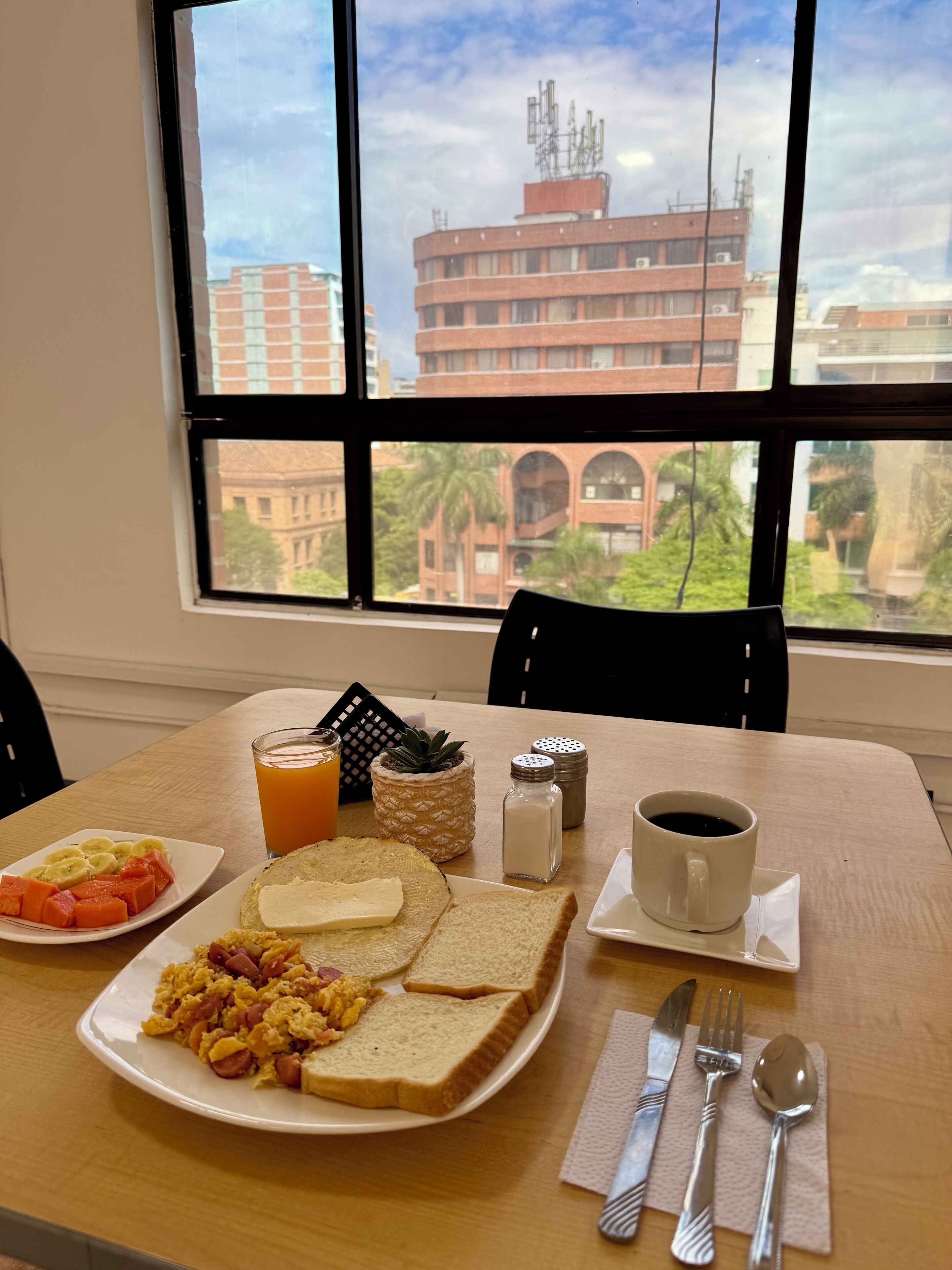 A breakfast table with plates of scrambled eggs, toast, and fruit, a glass of orange juice, and a cup of coffee.