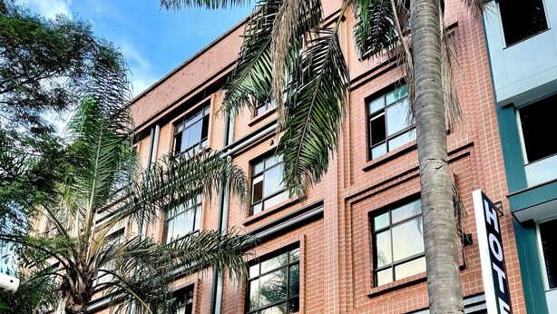 A multi-story building with a brick facade, a visible 'Hotel' sign, and a 'gana' store on the ground floor. - Hotel Plaza Mayor 44 - Medellin (Medellín)