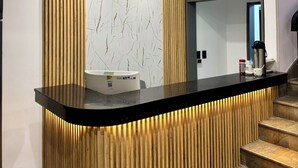 Un área de recepción con un mostrador curvo negro, pared con listones de madera y pared con estampado de mármol.