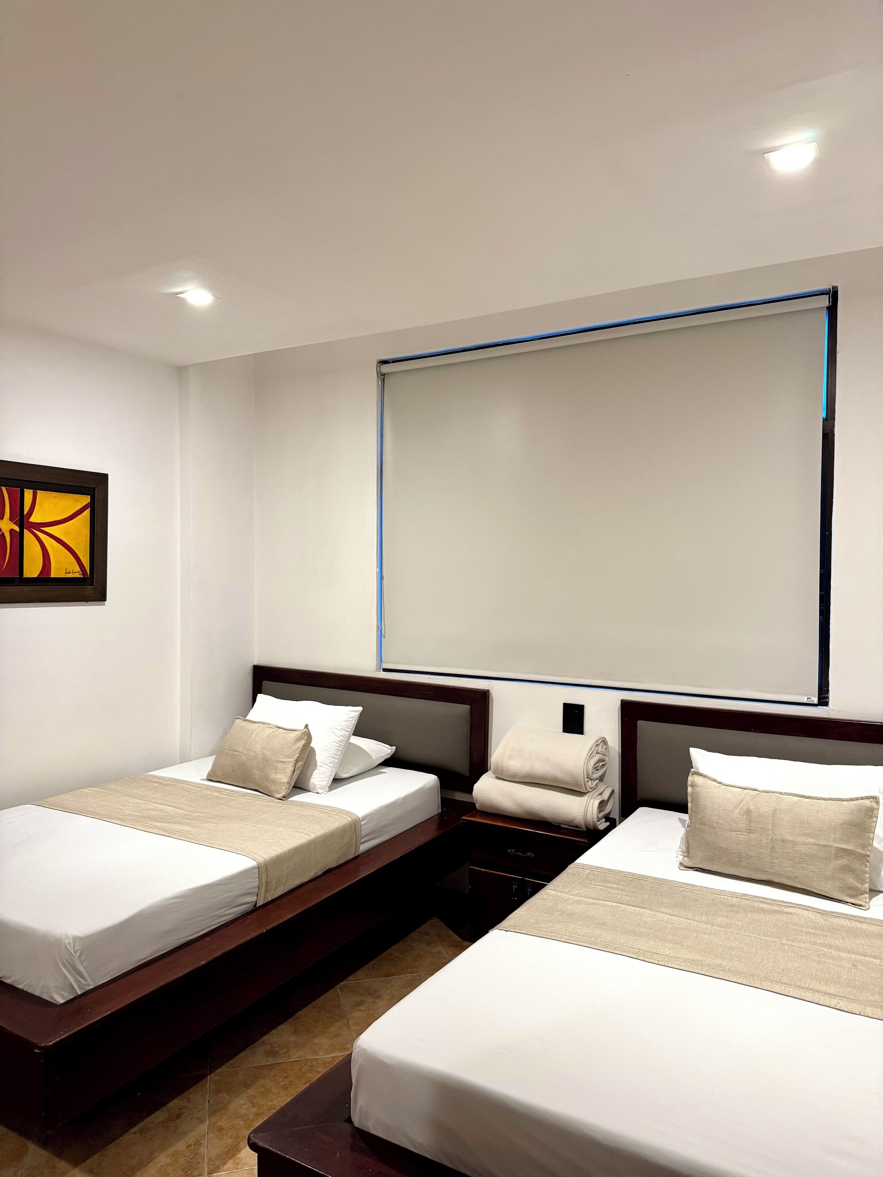 A hotel room with two beds, a large window, and a framed abstract painting on the wall.