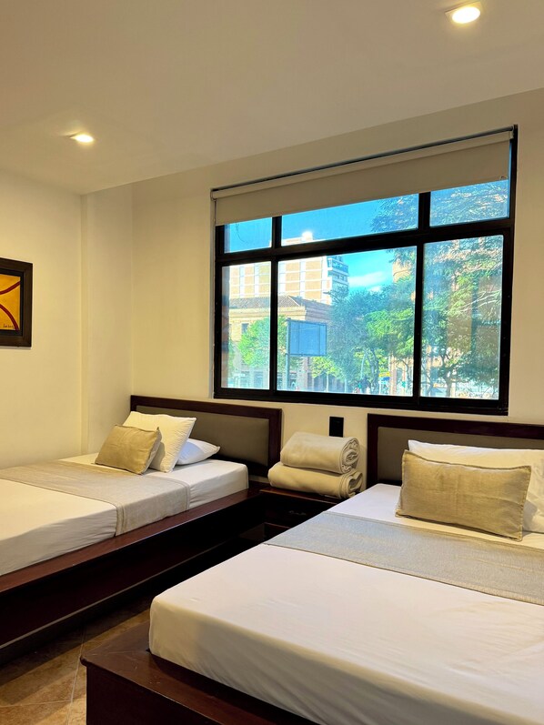 Habitación de hotel con dos camas, un ventanal con vistas a la ciudad y un cuadro en la pared.