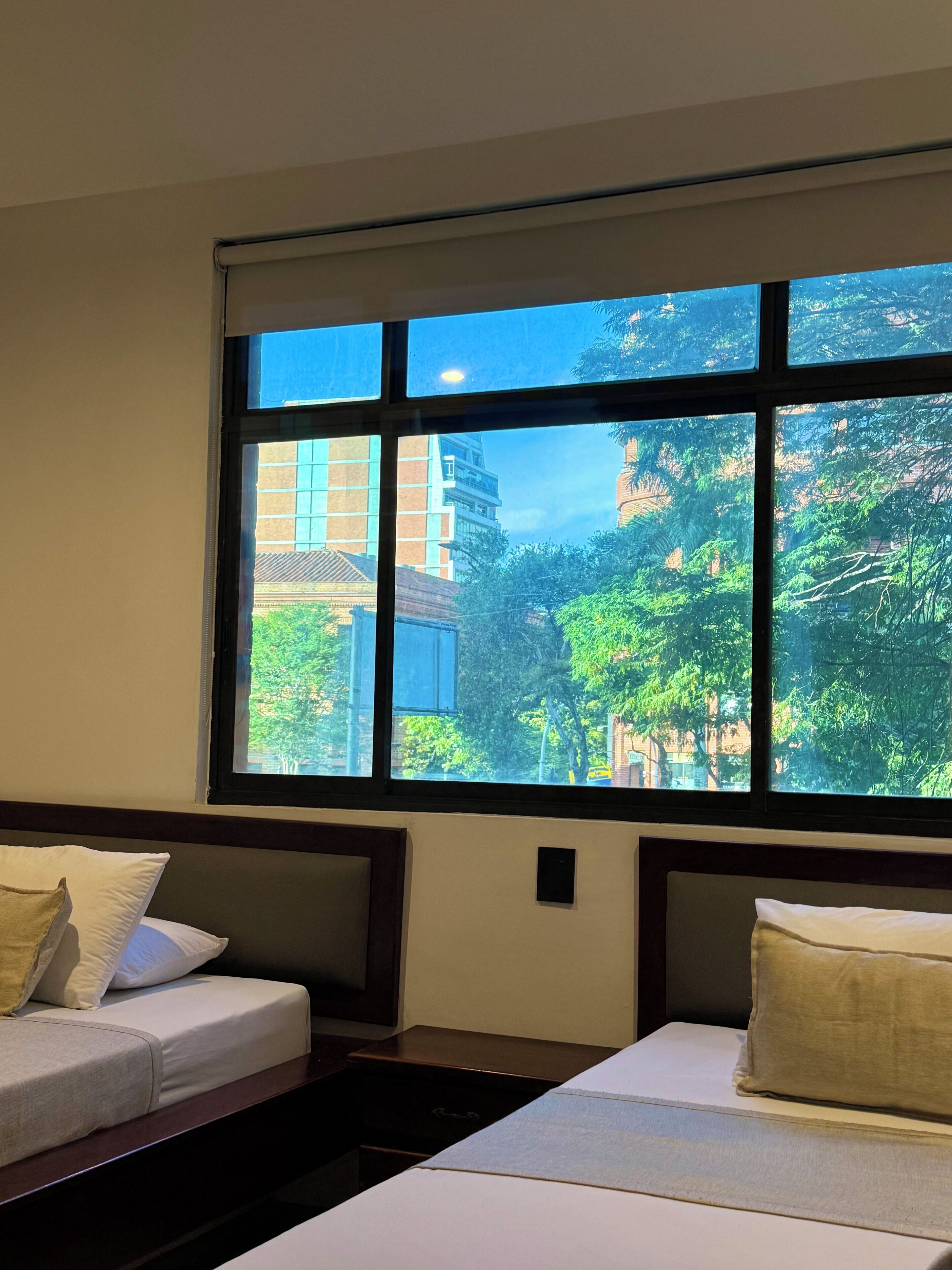 Habitación de hotel con dos camas, un ventanal con vistas a edificios y árboles.
