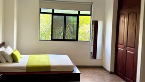 A bedroom with a bed, a window with a view of greenery, a wooden door, and a tiled floor. - Hotel Plaza Mayor 44 - Medellin (Medellín)