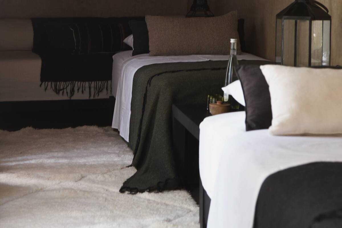 A room with two beds, a nightstand, a lantern, and a bottle on the nightstand.