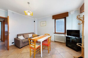A living room with a sofa, dining table, chairs, a TV, and a radiator.