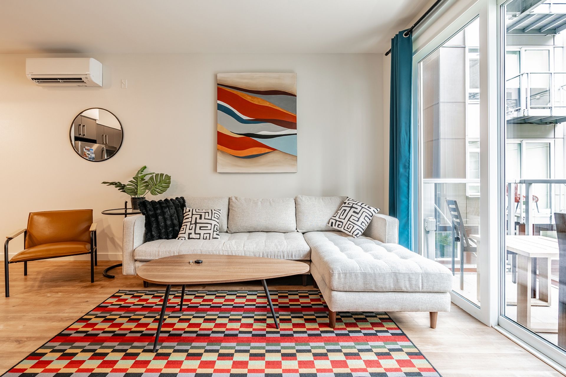 A modern living room with a sectional sofa, a round coffee table, a patterned rug, a potted plant, and a large abstract painting.