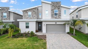 A modern two-story house with a stone facade, a garage, and a well-maintained lawn. - 9BR Lakeview Villa - Pool, Jacuzzi & Pool Table! (Kissimmee)
