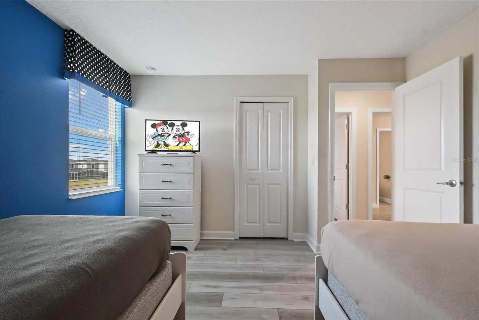 A bedroom with two beds, a dresser, a door, and a window with blinds.