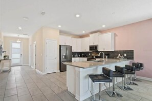 A modern kitchen with white cabinets, a stainless steel refrigerator, a microwave, and a large island with bar stools.
