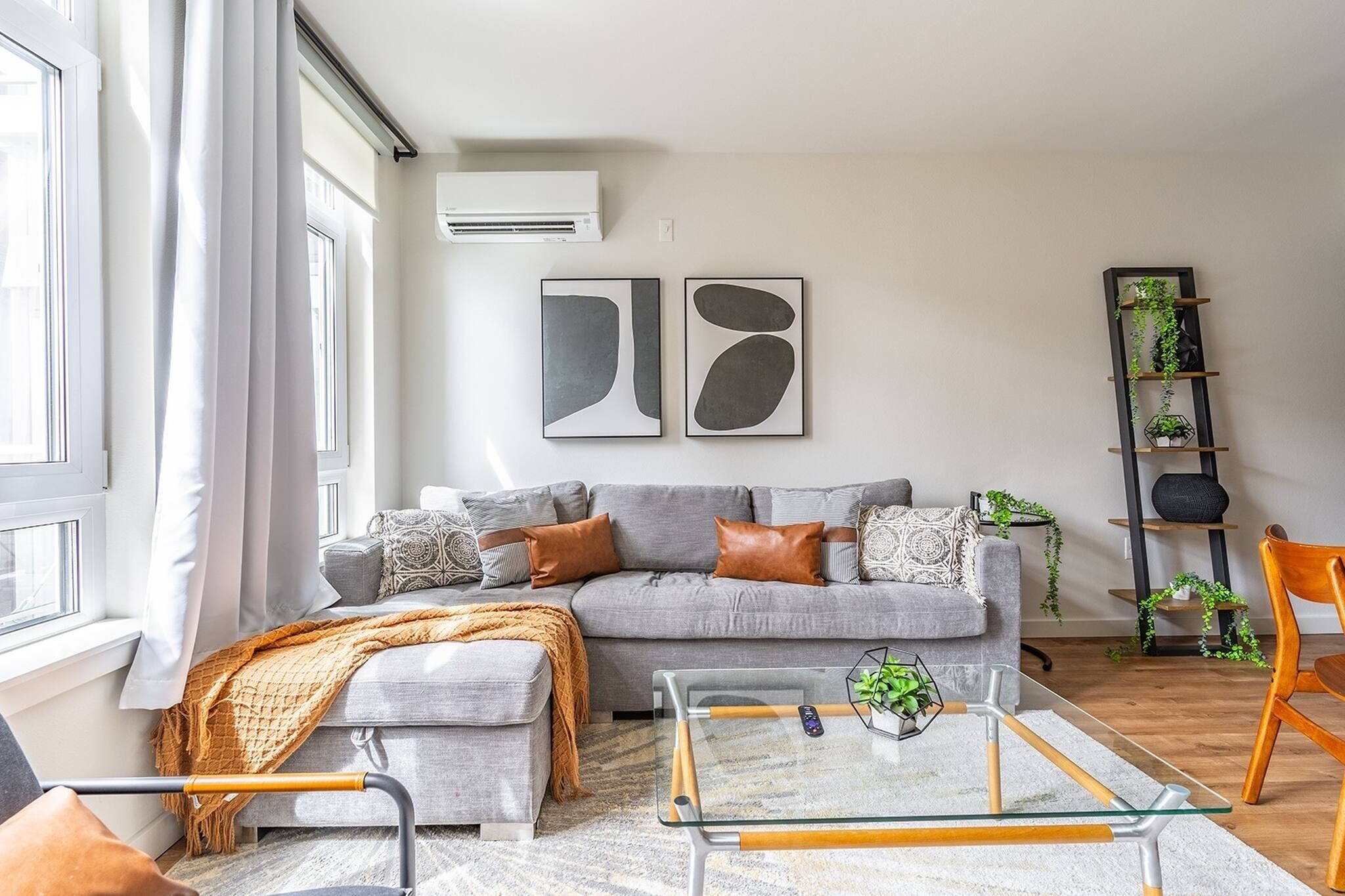 A modern living room with a grey sofa, a glass coffee table, and a plant shelf.