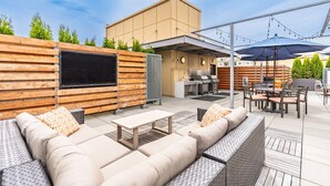 An outdoor patio with a TV, grill, and seating area. - 1BR | Gym, Views | Bellevue | Sophari Parkside C (Bellevue)