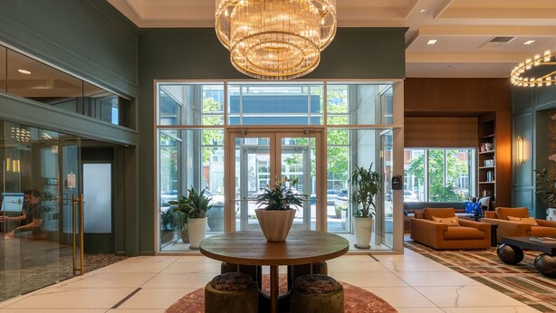 A lobby with a round table, potted plants, a chandelier, and a large glass door leading outside. - 1BR | Gym, Views | Bellevue | Sophari Parkside C (Bellevue)